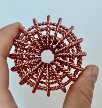 Hand holding a metallic copper-colored crochet doily against a light blue background