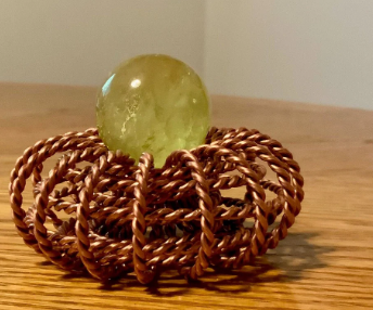 Decorative copper woven ring charging a crystal on a wooden surface