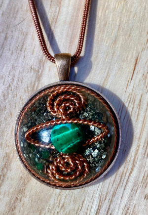 Pendant with green stone and copper wirework on a wooden surface