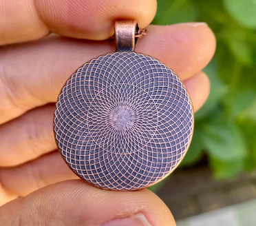 Close-up of a hand holding a round pendant with intricate design against a blurred green background