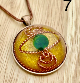 Round pendant with a green gemstone and braided design on a wooden surface