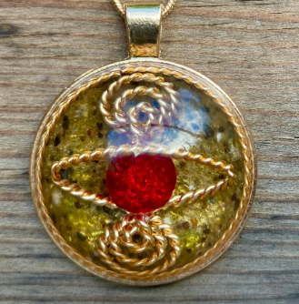 Gold pendant with a red stone and intricate design on a wooden surface