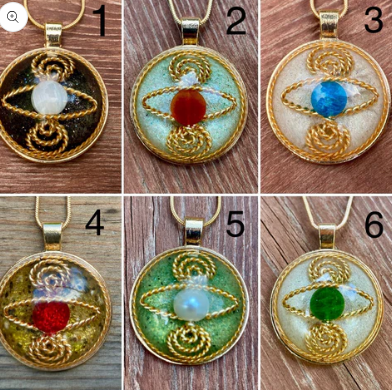Six gold-framed pendant designs with various central stones on a wooden surface.