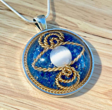 Pendant with blue stone, gold accents, and white pearl on a wooden surface