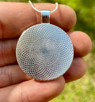 Silver textured pendant held in a hand with a blurred green background