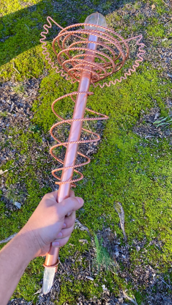 Rose gold spiral object held by a hand on a green mossy background