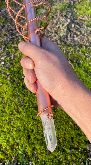 Hand holding a crystal with a rope against a grassy background
