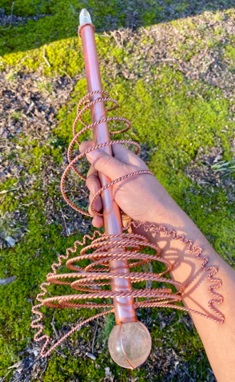 copper crystal wand held by a hand against a natural background