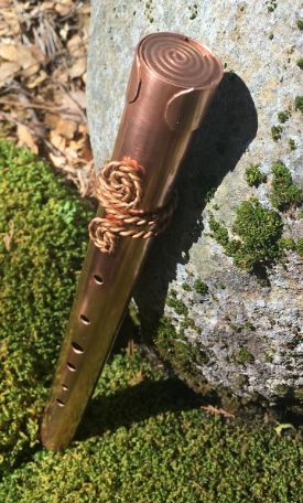 Copper flute with decorative elements on a stone and moss background