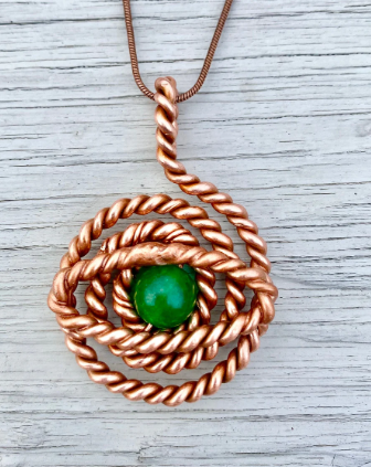 Copper spiral pendant with a green bead on a wooden surface