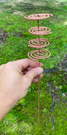 Hand holding a copper spiral object against a green grass background