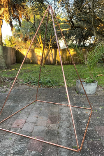 Copper geometric frame on a stone patio with trees in the background
