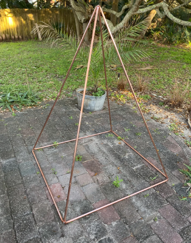 Copper pyramid golden ratio on a patio with grass and trees in the background