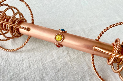 Copper rod with embedded gemstones on a textured surface