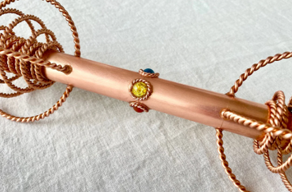 Copper rod with embedded gemstones on a textured surface