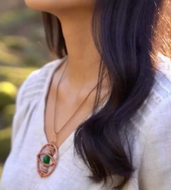 Person wearing a necklace with a green stone, blurred background