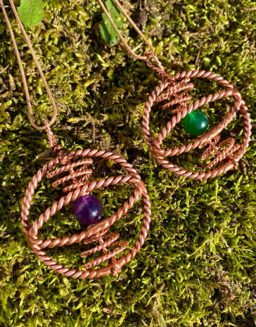 Two copper wire-wrapped pendants with gemstones on a moss background