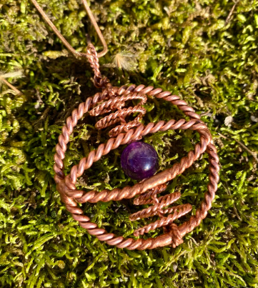 Copper wire-wrapped pendant with a purple gemstone on a green moss background