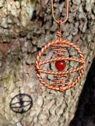 Copper necklace with a red stone against a tree bark background