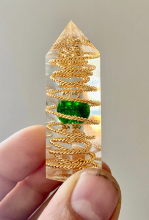 Crystal with gold spiral design held by a hand against a neutral background
