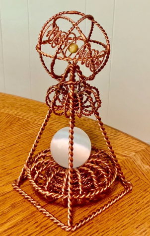 Copper wire sculpture with a white sphere on a wooden surface