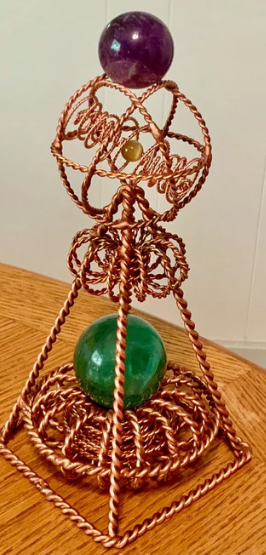 Copper wire sculpture with amethyst and green stone on a wooden surface