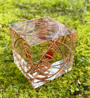 Decorative glass cube with copper sacred geometry design on a grassy background