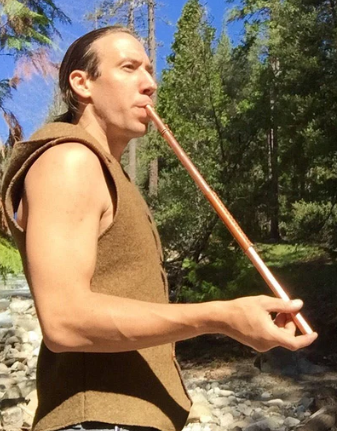Person playing a copper flute in a forest setting