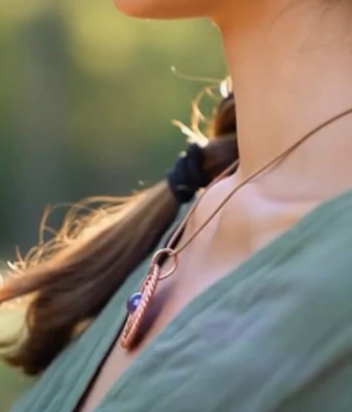Close-up of a person wearing a necklace with a blurred natural background