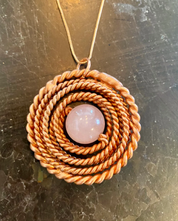 Pendant with pink stone and braided design on a metallic surface