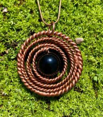 Copper spiral pendant with a black stone on a green moss background