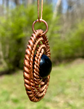 Copper woven pendant with a black stone against a natural background