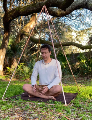 Man meditating under a tree with a pyramid-shaped object in a natural setting