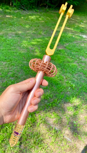 Hand holding a metallic tool with a decorative bow on a grassy background