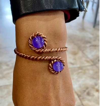 Copper bracelet with purple stones on a wrist against a blurred background