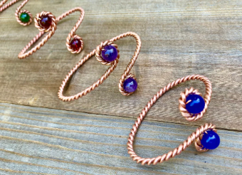 Copper wire earrings with blue and red beads on a wooden surface