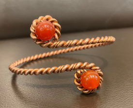 Copper bracelet with orange beads on a gray surface