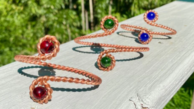Copper bracelets with embedded gemstones on a wooden surface