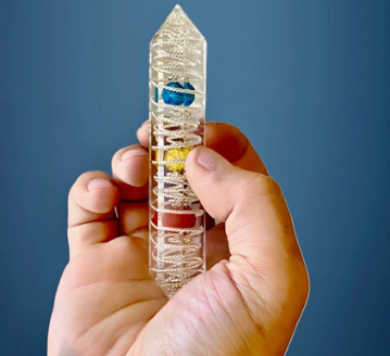Crystal tower with colored stones held by a hand against a blue background
