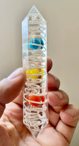 Crystal wand with colorful embedded stones held in a hand against a neutral background