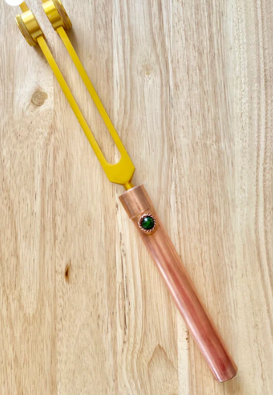 Yellow tool with a pink handle and green gemstone on a wooden surface