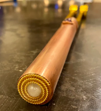 Copper rod with gold wrapping on a dark surface