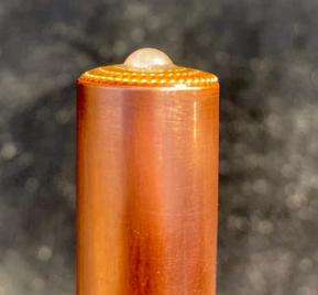 Wooden cylindrical object with a textured top on a dark background