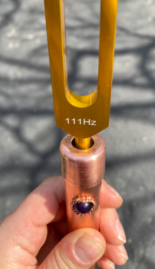 Tuning fork with '111Hz' marking held by a hand against a textured background