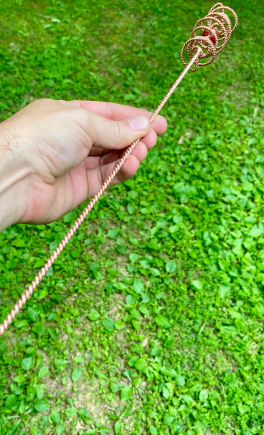 Hand holding a coiled copper wire against a grassy background