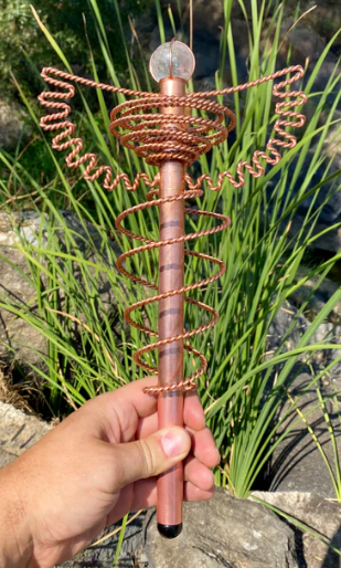 Copper spiral tool held by a hand with grass and water in the background