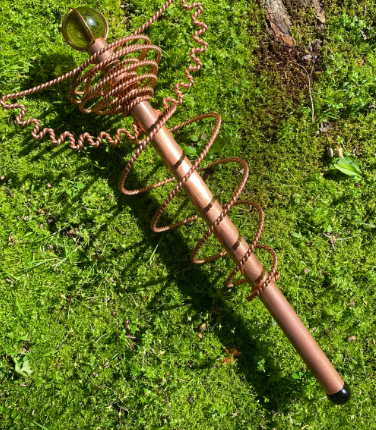 Copper wand with a green gemstone on a mossy background