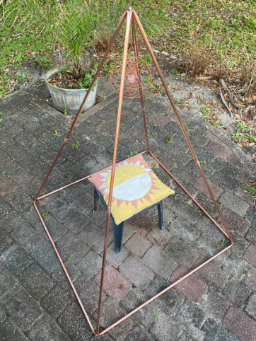 Copper golden ratio pyramid on a stone patio with a small stool underneath