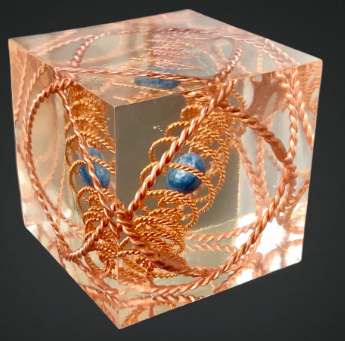 Decorative cube with intricate copper wirework and blue stones on a dark background