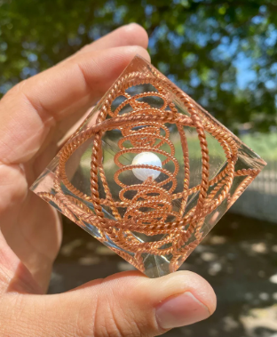Hand holding a transparent cube with intricate copper wire patterns against a blurred natural background